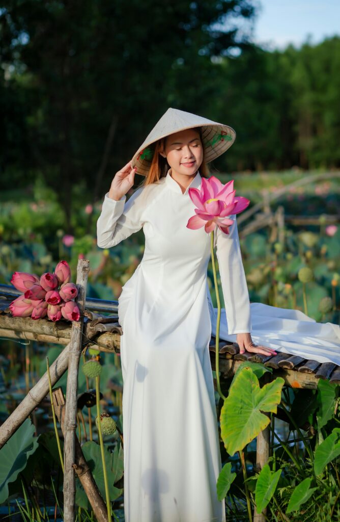 A woman in a white ao dai holding a lotus blossom in a serene lotus field.
